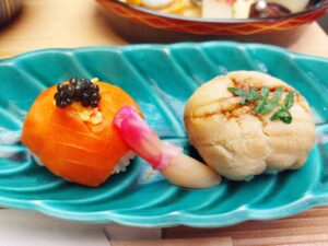青っぽい細長い皿にサーモンと穴子の手毬寿司が1貫ずつ載っている。中央には生姜