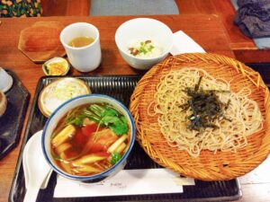 ザルに載ったそばと、つけつゆ、薬味、御飯の写真