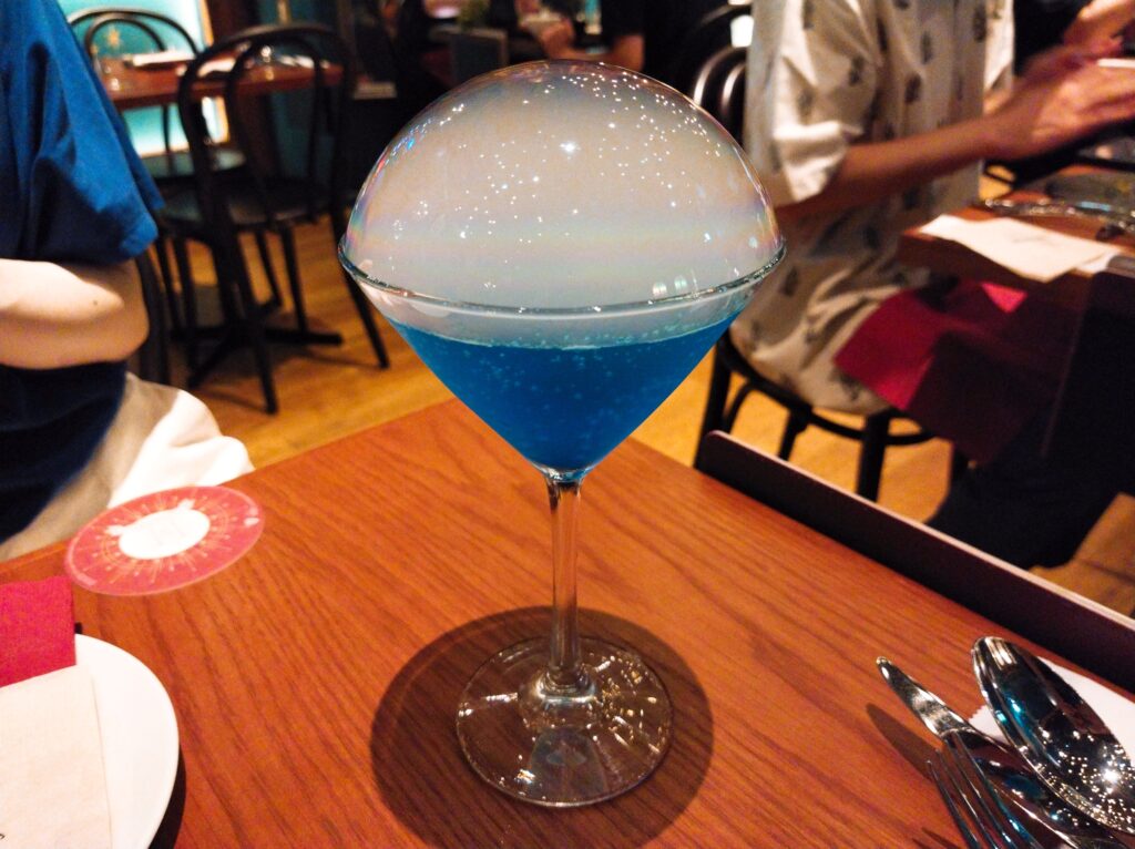 ショートグラスに入った青いドリンクを大きなひとつの泡が覆っている
